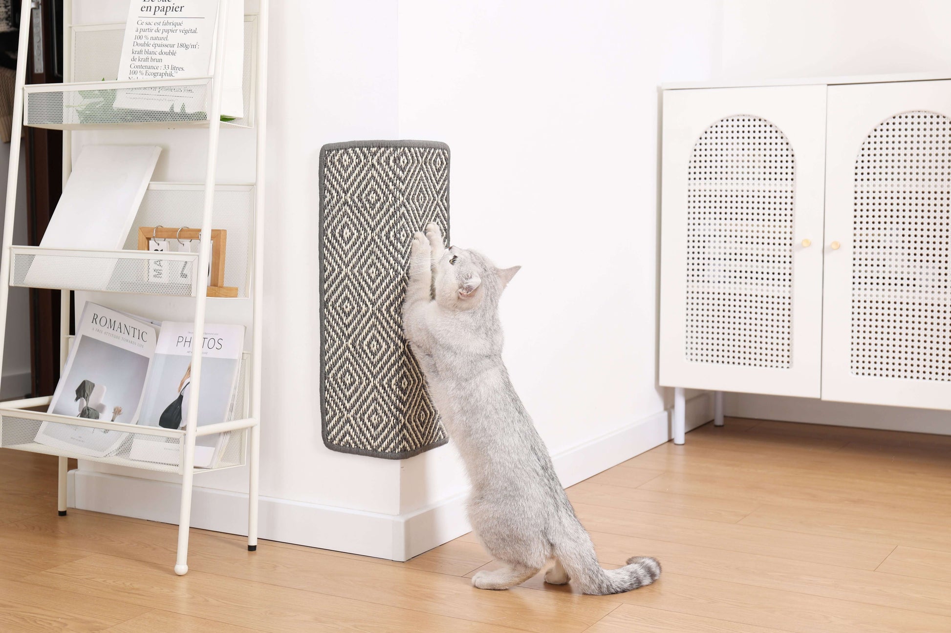 Cat using boho-style natural sisal scratching mat attached to wall in modern living room.