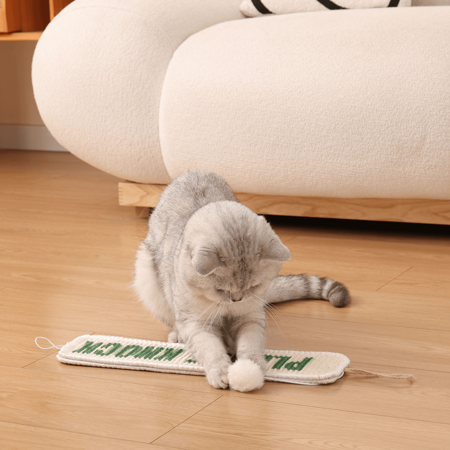 Cat playing with Furrther's 3-in-1 Hanging Sisal Scratch Mat featuring catnip ball on wooden floor.